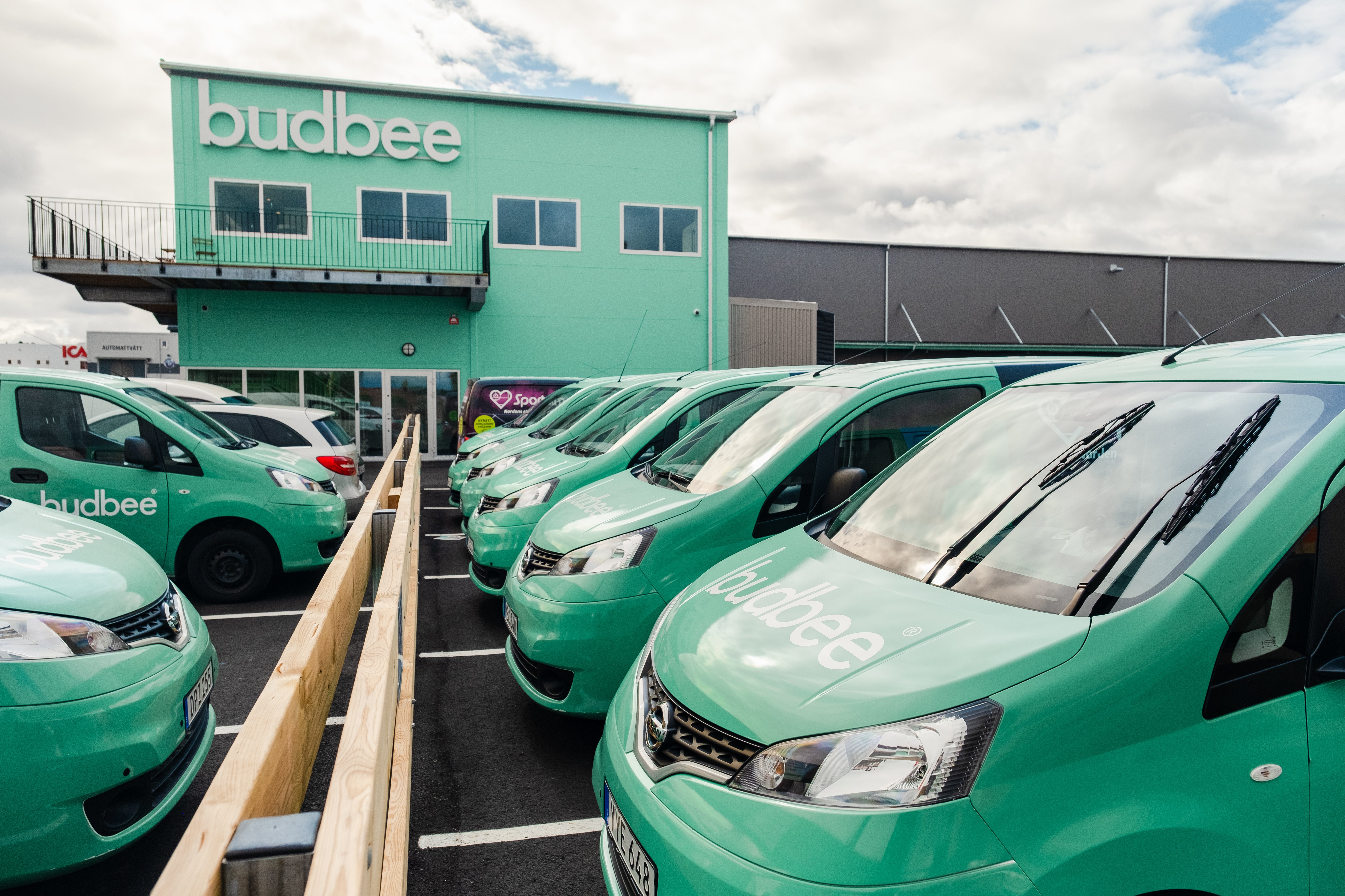 Row of green vans parked outside a building with 'budbee' branding.