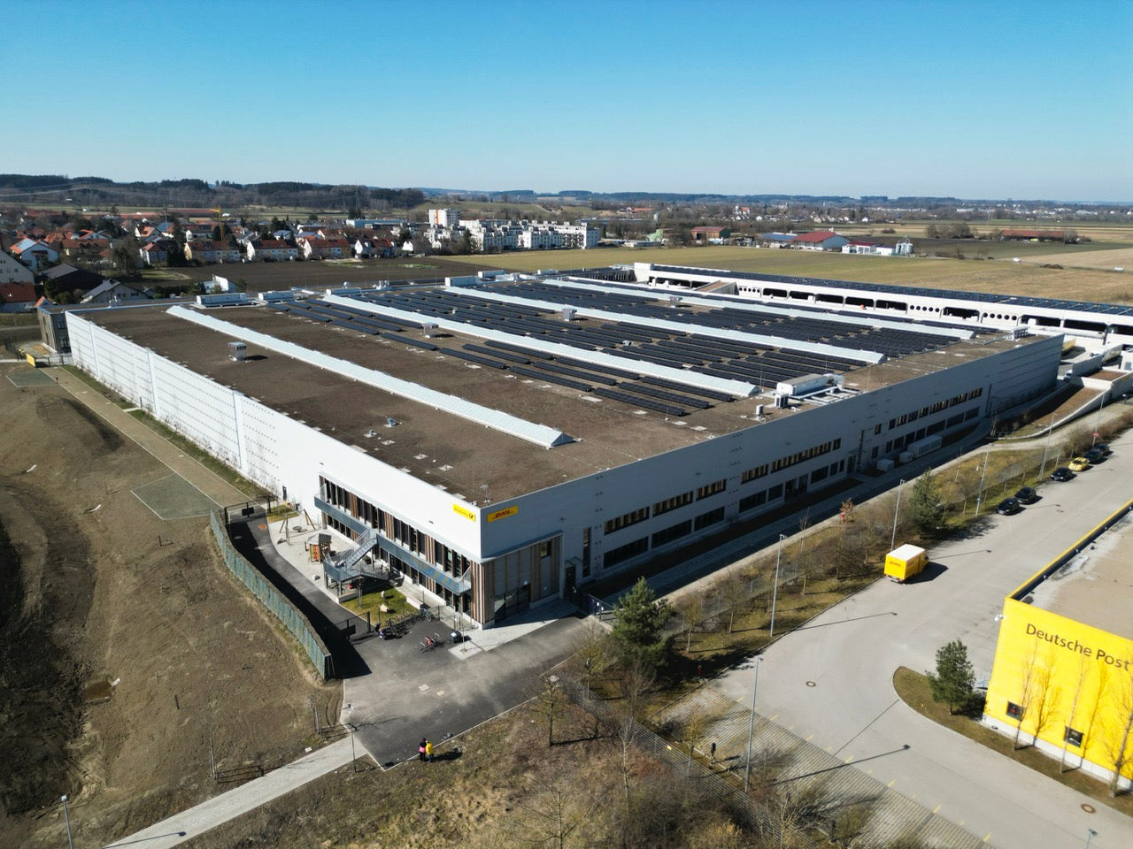 Large industrial building with solar panels on the roof, surrounded by a clear sky.