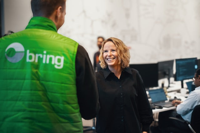Person wearing a green 'bring' vest interacting with another person in an office setting.