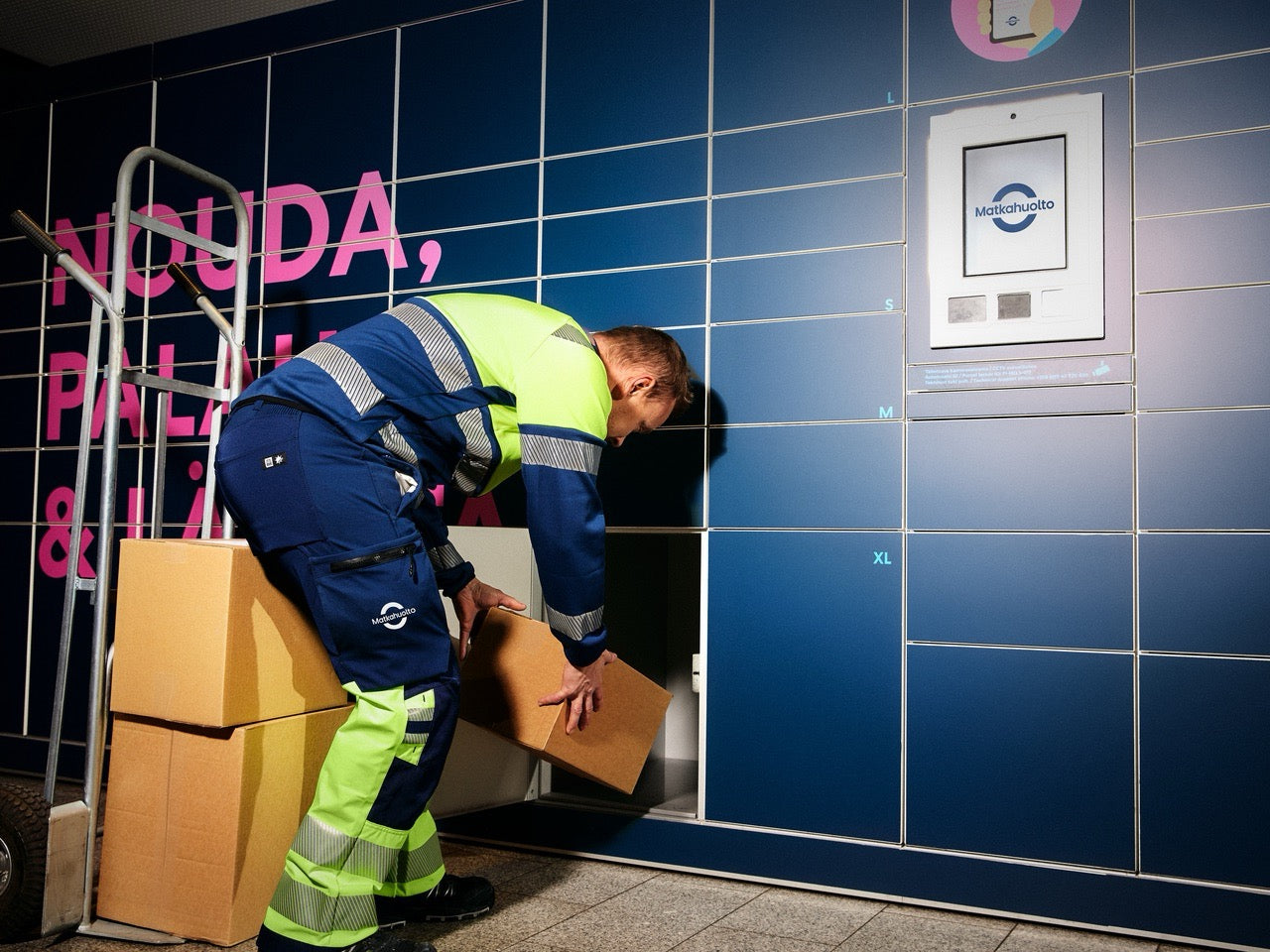 Person in high-visibility clothing interacting with a Matkahuolto parcel locker